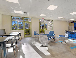 The break room with its chairs and tables hitting sunlight from the two glass doors and windows against the wall.