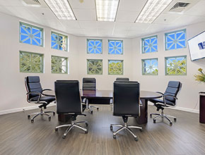 A large conference room with a large table and six chairs, illuminated by square windows group by four on each outside facing wall.