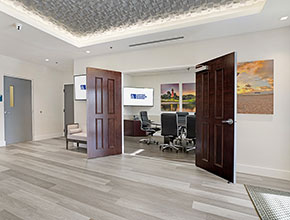 A wooden floored lobby with the double doors to the conference room open to view the small table with six chairs