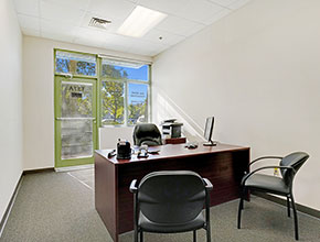 An executive suite office with a desk with three chairs, and a glass door and window to the street.