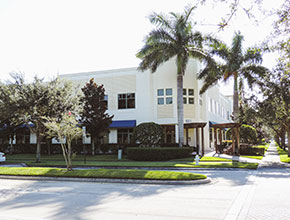 The outside main entrance for a two story business center with some palm trees and overhangs