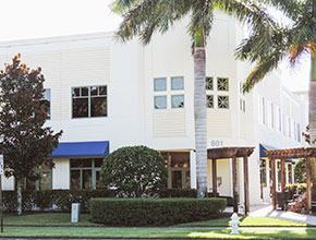 The outside main entrance for a two story business center with some palm trees and overhangs